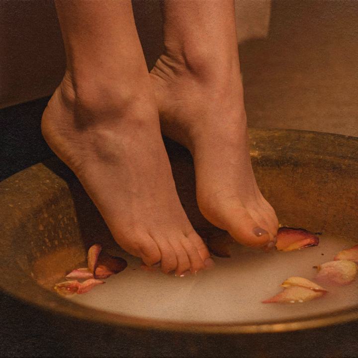 woman dipping her feet into a bowl of water with flower petals in it